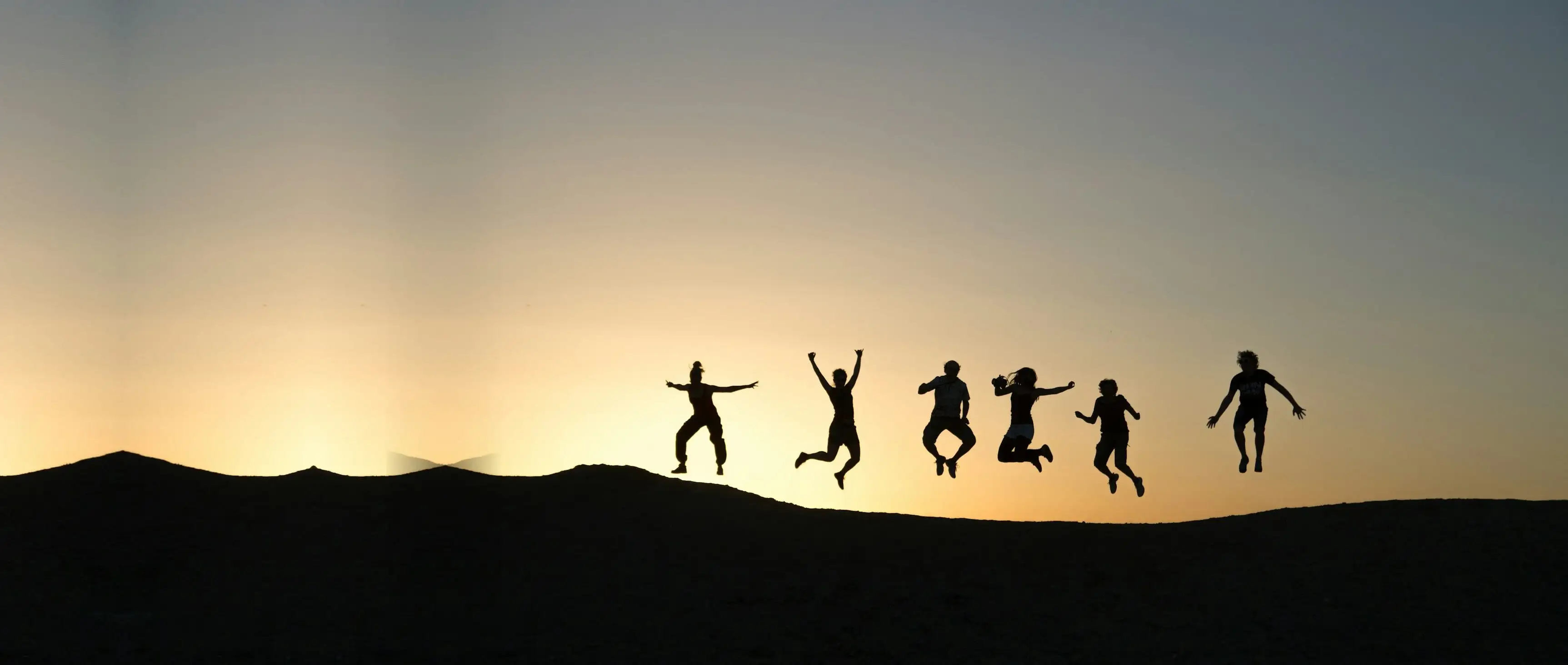 Silhouetten von sechs Menschen, die im Sonnenaufgang gemeinsam in die Luft springen